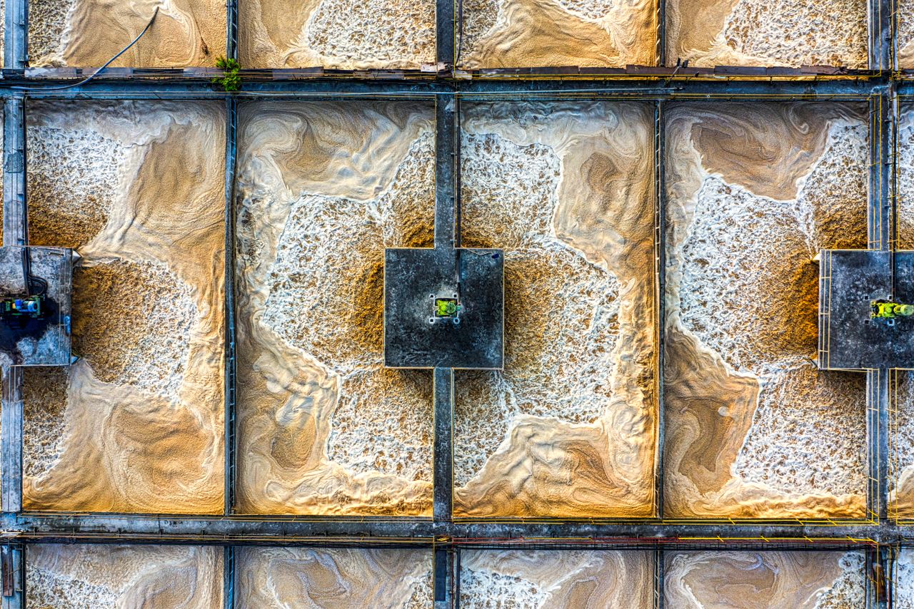 Drone shot of a wastewater treatment plant showcasing intricate grid patterns and swirling water.